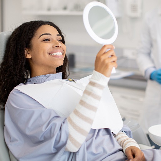 Woman smiling at reflection in handheld mirror