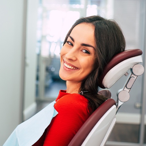 Woman in red shirt sitting in dental chair and smiling