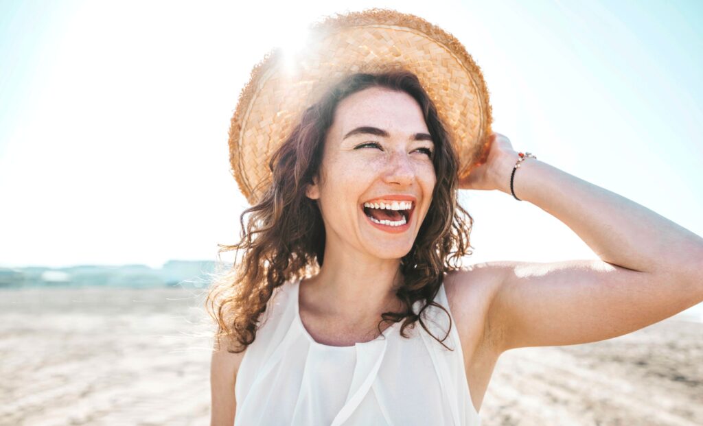 Woman at beach smiling holding hat on head